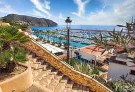 An elevated, scenic view from stone stairs overlooking a sunny, busy marina filled with yachts and turquoise water, with a hilly coastline in the distance. This aspirational image, used by a crypto learning platform, symbolizes the high returns and financial freedom achievable by mastering decentralized finance and focusing on crypto learning and cryptocurrency investment.