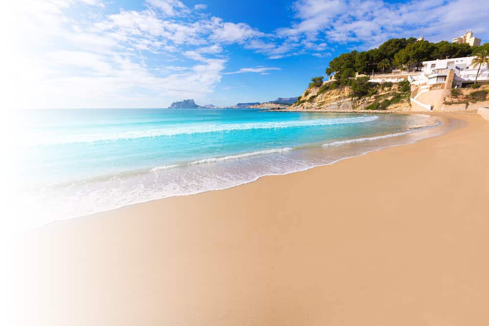Stunning wide-angle view of a sunny, crescent-shaped beach with clear turquoise water, a sandy shoreline, and white houses on a low cliff in the distance. This aspirational lifestyle image, used by a crypto learning platform, symbolizes the financial freedom and remote work achievable by mastering decentralized finance and learning cryptocurrency skills.